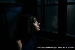 Young woman dreamily looks outside of window in house at night 4mWlv0