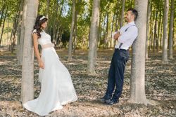 Newlywed man and woman facing each other while leaning on trees