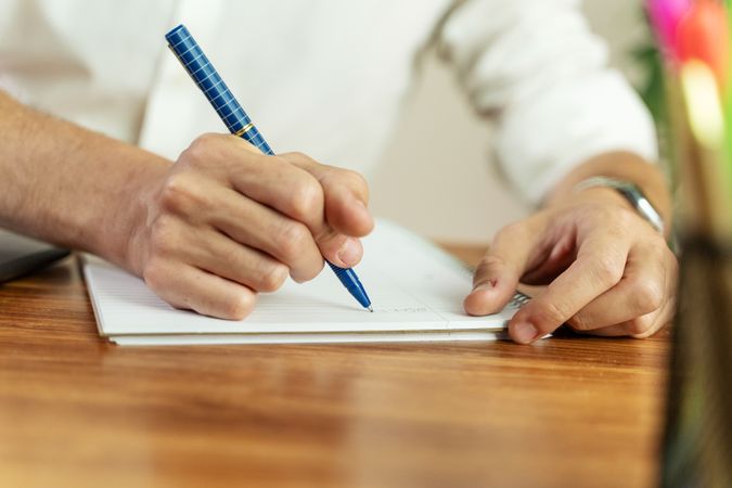 Close-up of a man's hand writing notes in a notebook at a desk.