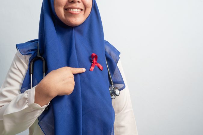 Happy Muslim Female Asian doctor or nurse pointing Red ribbons on cloth, HIV awareness concept, world AIDS day, world cancer day.