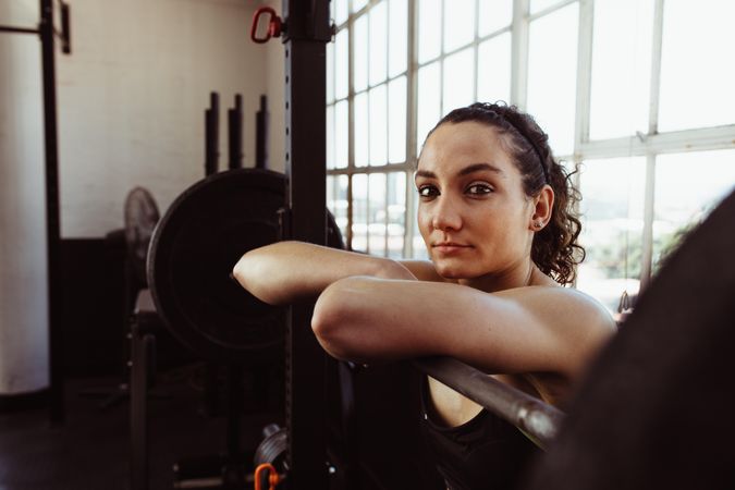 Young woman leaning over barbell after training in gym