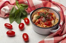 Bowl of delicious ravioli with tomato sauce and rosemary on table cloth