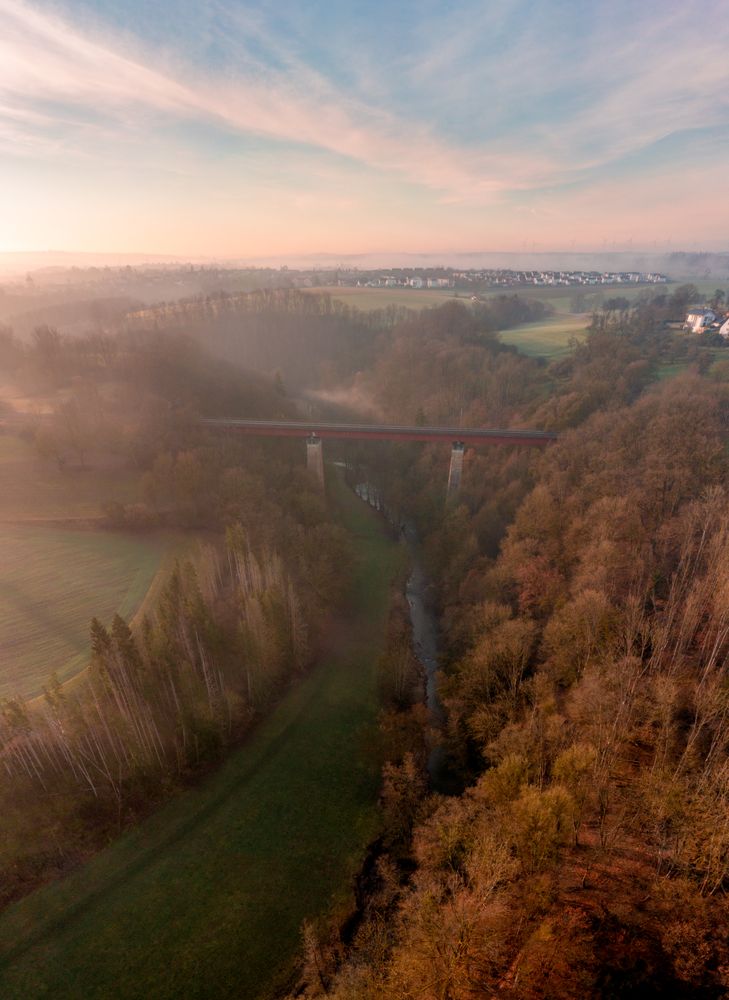 Railway bridge crossing river in winter nature, drone shot at sunrise