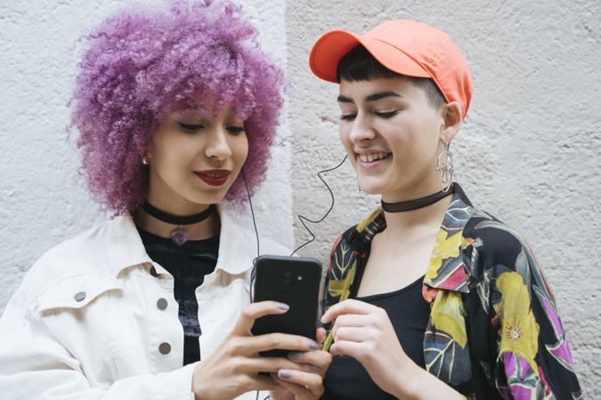 Bright women bonding and looking at mobile phone on street