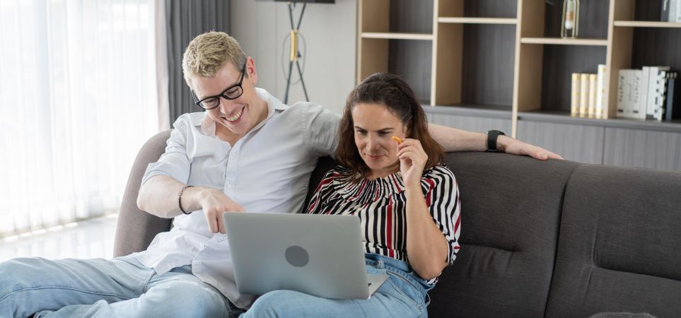 Laughing couple talking and looking on laptop together in the living room
