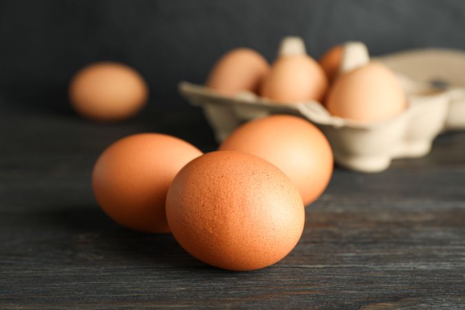 Brown chicken eggs in carton box on wooden table against dark background, space for text and closeup