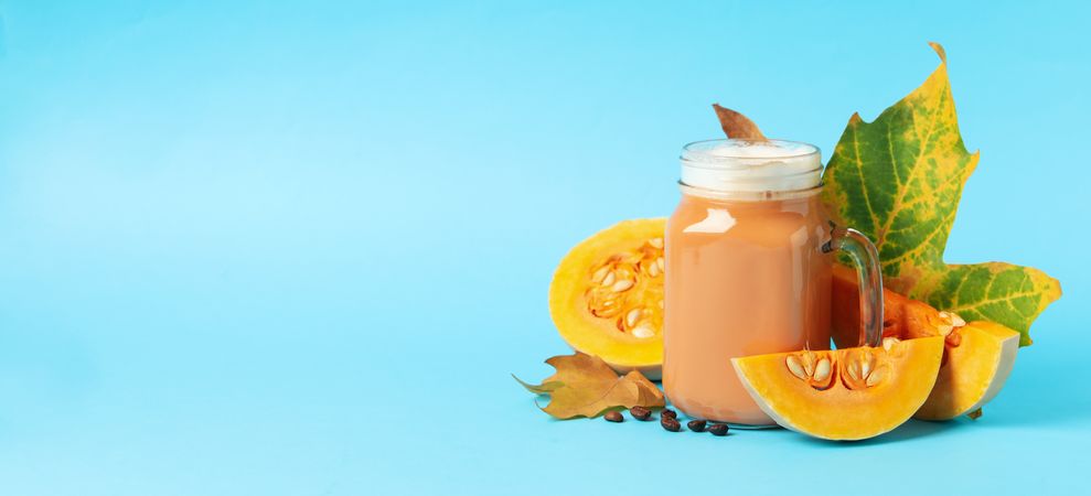Composition with glass jar of pumpkin latte on blue background