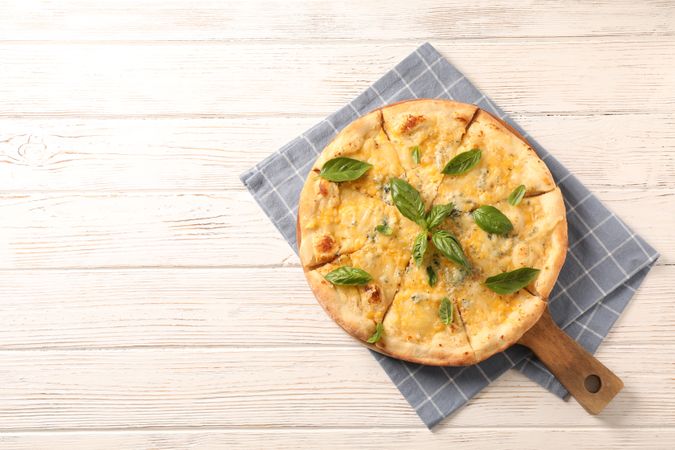 Towel, board, cheese pizza with basil on wooden background, copy space