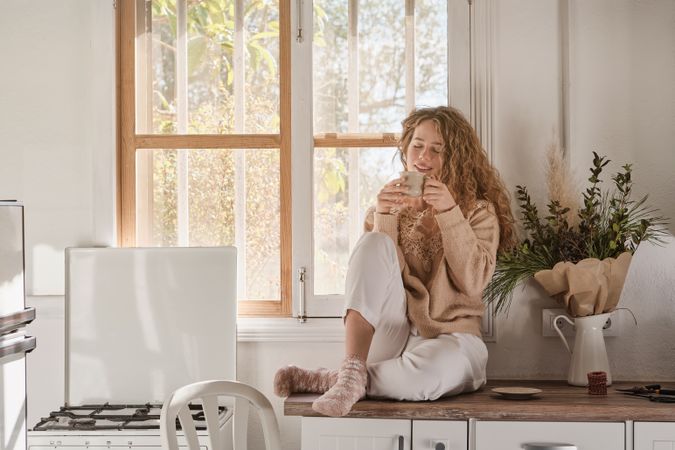 Young woman drinking hot beverage in kitchen