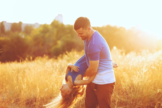 Man playfully carrying daughter through field