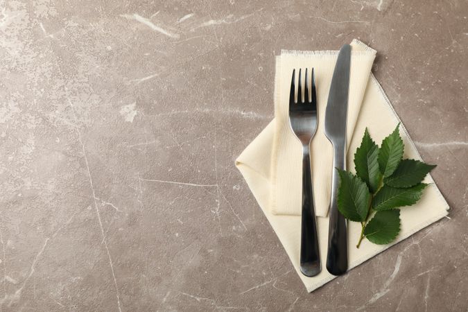 Napkin, cutlery and leaves on gray background, space for text