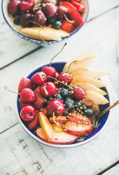 Top view of blue bowls of fresh fruit with cherries, peaches, blueberry