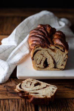 Fresh twisted bread or cinnamon babka over wooden table with striped towel on blurred background