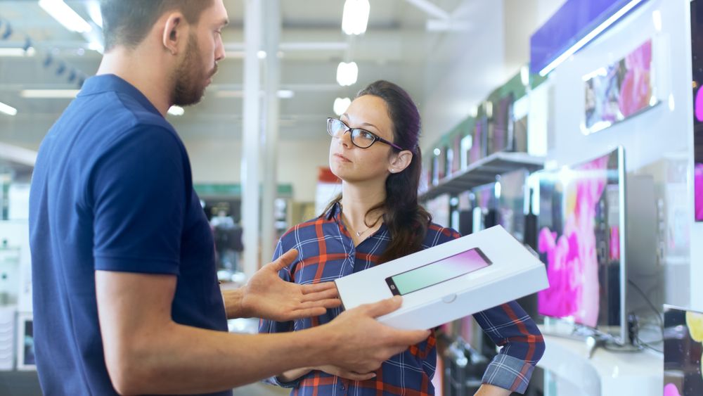 In the Electronics Store Professional Consultant Provides Expert Advice on Tablet Computer Specifications For Young Woman.