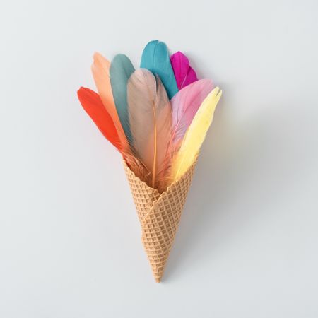 Colorful feathers in waffle cone on light background