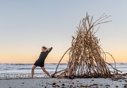Young woman dancing on shore near water and wooden twigs placed for campfire