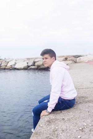 Young pensive teenager male sitting on breakwaters while looking at camera