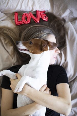Woman lying on the bed holding her dog and a red love balloon above her head