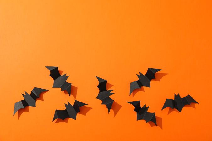 Flat lay with decorative bats on orange background, copy space