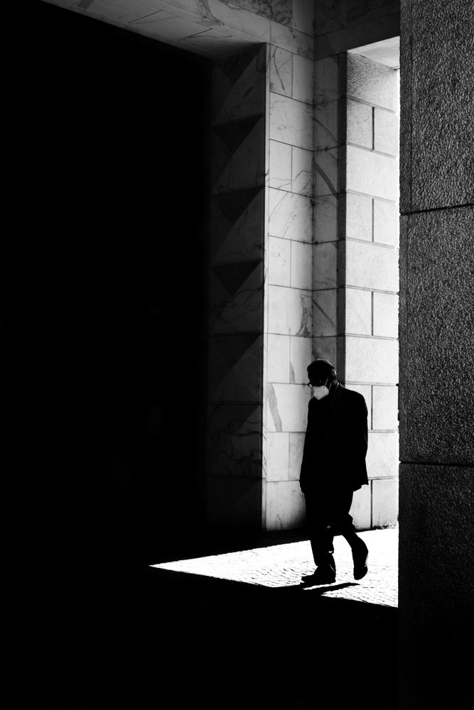 Older man with head down walking through tall door