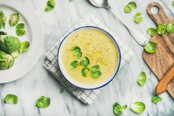 Brussels sprout soup, garnished with fresh sprouts, next to wooden board