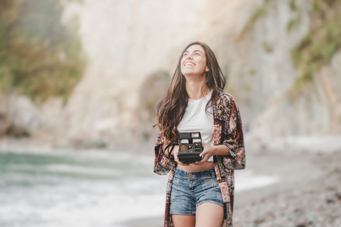 Woman with camera on shore near stones and water