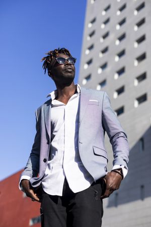 Looking up at Black man in elegant suit standing on a sunny street against a blue sky