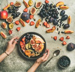 Woman holding bowl of yogurt over table of figs, peaches, and chia seeds, square crop