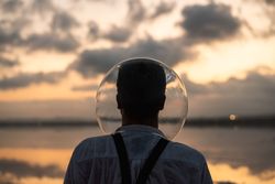 Man with fish tank on head standing at seashore