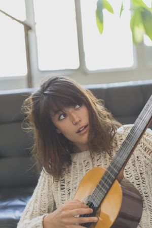 Female in wooly sweater looking at fretboard of guitar