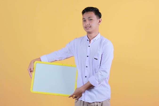 Portrait a young man in yellow backdrop holding a blank note board