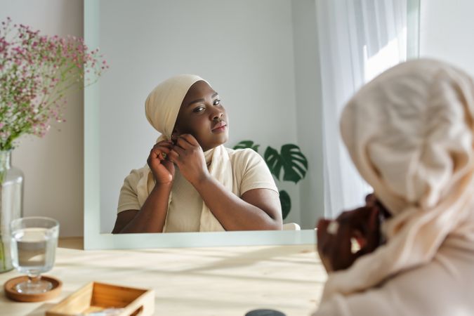 Dreamy Black woman looking in mirror and putting on earring