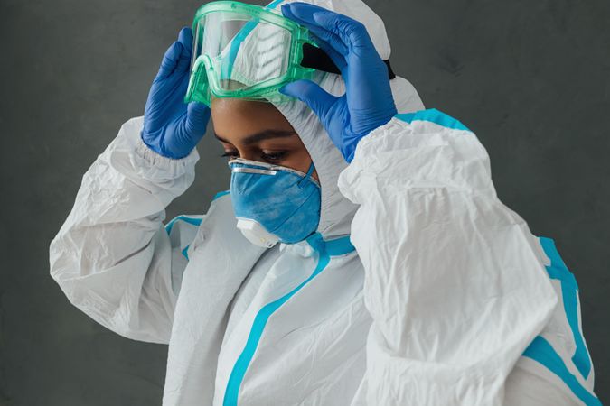 Side view of Black female medical worker adjusting her PPE goggles