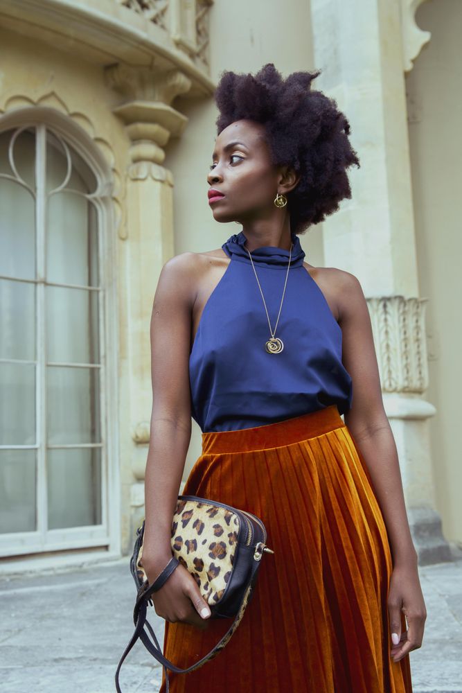 Woman in blue shirt and brown skirt holding a handbag looking away