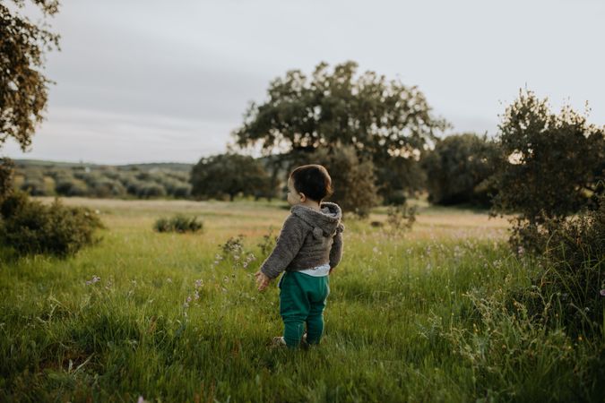 A young boy standing alone in a field surrounded by trees