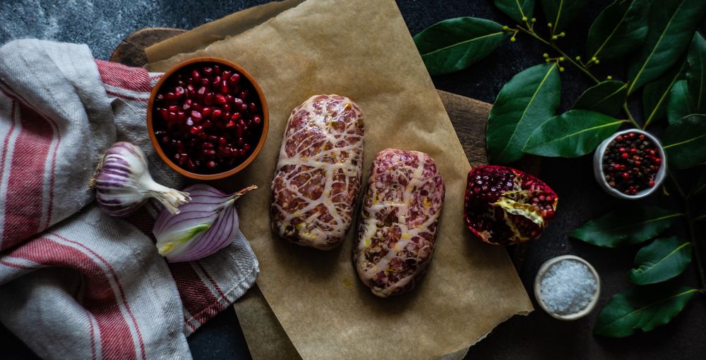 Top view of raw abkhazura meat cutlets with pomegranate seeds & bay leaves
