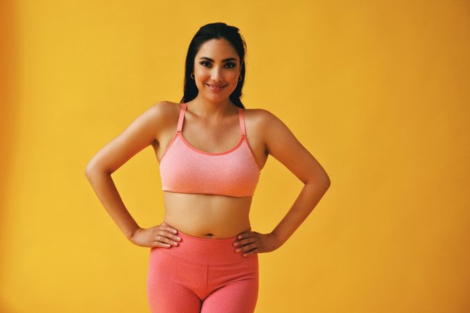 Hispanic woman in yoga clothes with hands on hips in yellow room, copy space