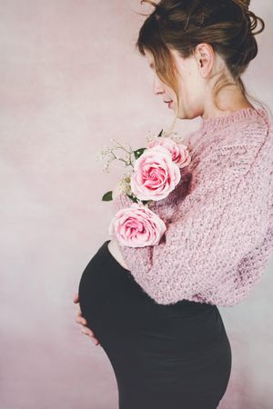 Side view of pregnant woman in pink knit sweater holding pink rose bouquet