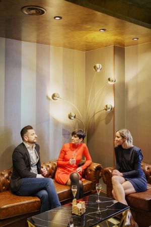 Group of friends enjoying drinks on leather sofa’s in lounge, vertical