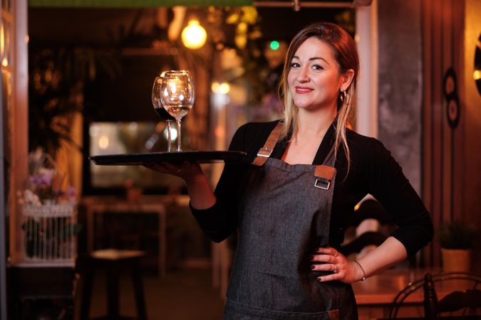 Cheerful waitress holding tray with wineglasses