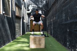 Concentrated athlete jumping on wooden box