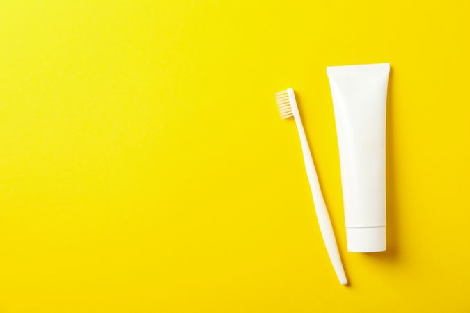 Toothbrush and toothpaste on yellow background, space for text