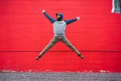 Bearded guy jumping near red wall
