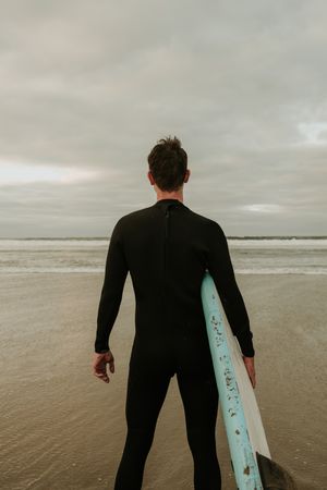 Person with surfboard standing near sea