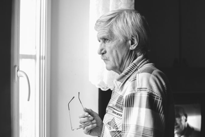 Grayscale photography of older man standing front of window