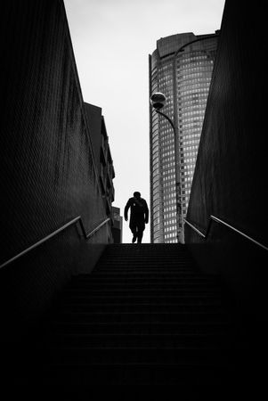 Back view of man climbing an outdoor staircase in grayscale