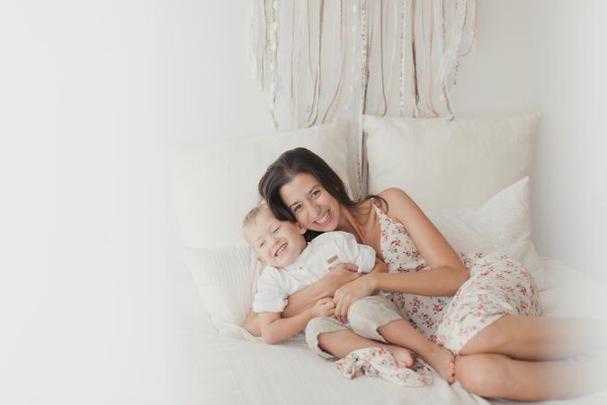 Mother ticking little son and laughing on bed