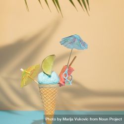 Blue ice cream in cone with several cocktail parasol and sunglasses on beach background 0Kqjy4