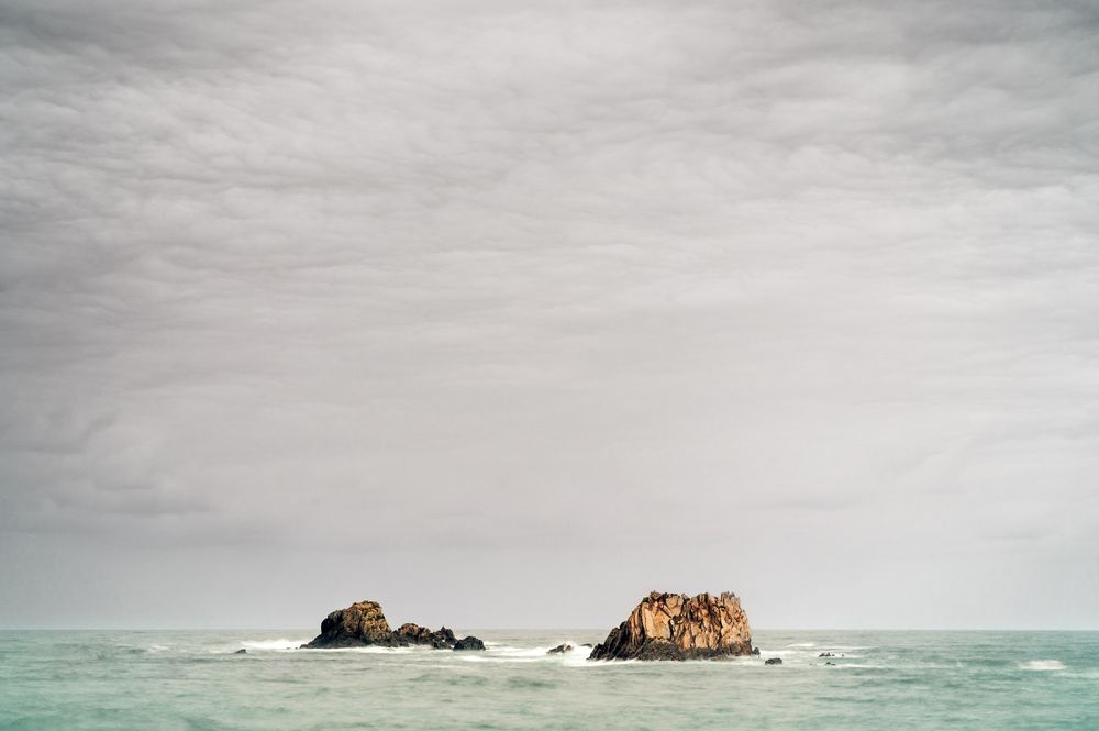 Rocky peaks protrude from water in cloudy day