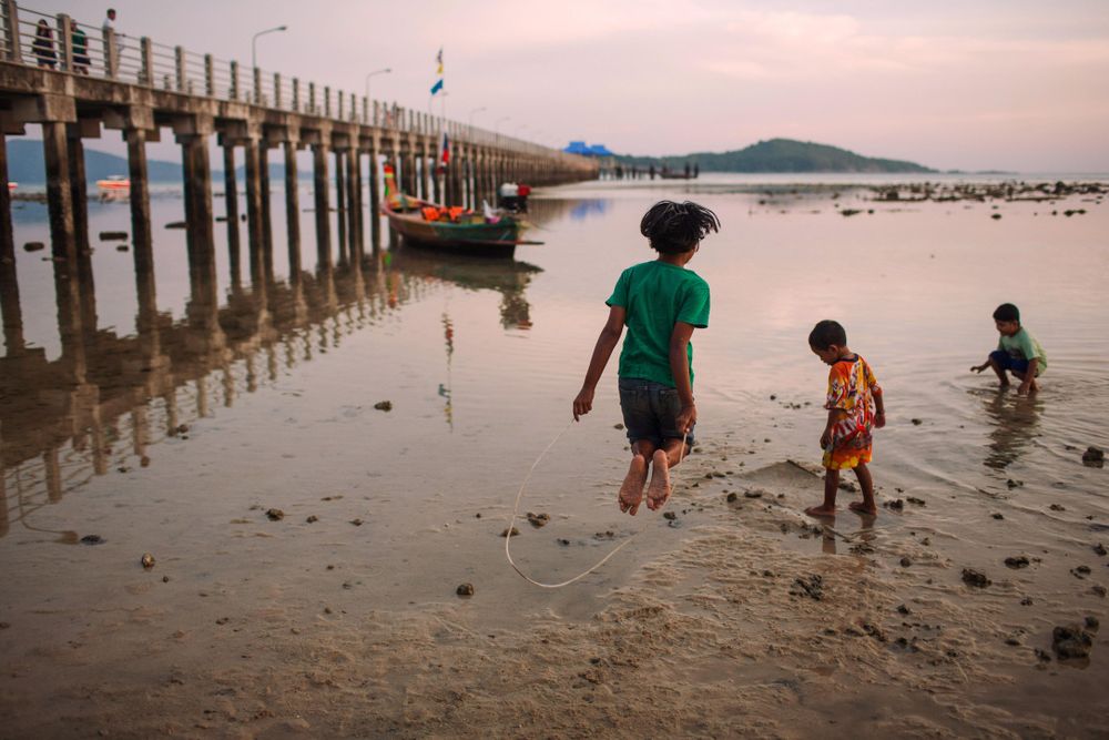 Back view of children playing by shoreline near piers at sunset